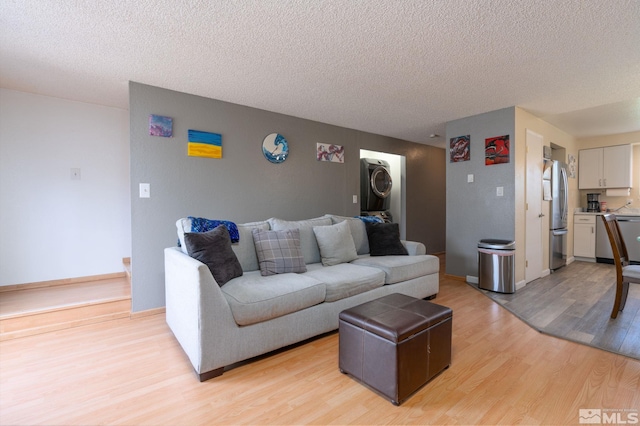 living room with light hardwood / wood-style floors, stacked washing maching and dryer, and a textured ceiling