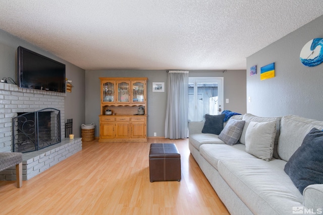 living room with wood-type flooring, a textured ceiling, and a brick fireplace