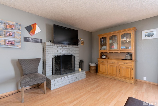 living room with a textured ceiling, light hardwood / wood-style floors, and a brick fireplace