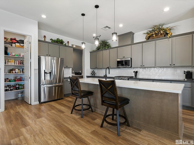 kitchen featuring hardwood / wood-style floors, hanging light fixtures, a kitchen island with sink, and appliances with stainless steel finishes