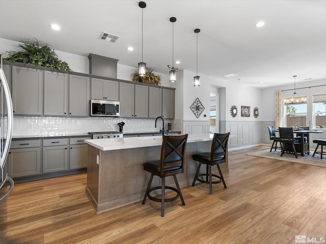 kitchen featuring hanging light fixtures, a breakfast bar area, a kitchen island with sink, appliances with stainless steel finishes, and light wood-type flooring