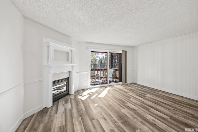 unfurnished living room featuring hardwood / wood-style flooring, a textured ceiling, and a tiled fireplace