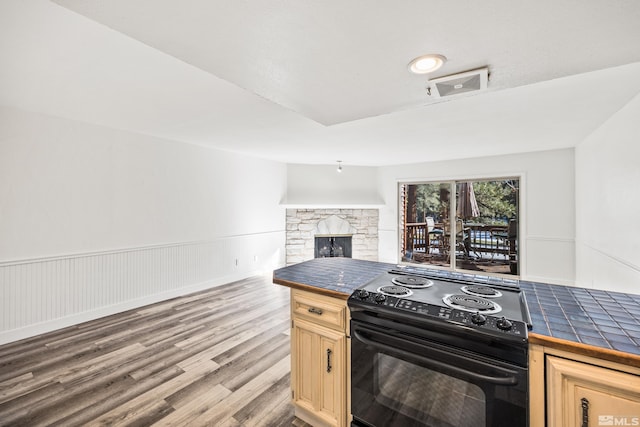 kitchen featuring light wood-type flooring, light brown cabinets, a fireplace, black electric range oven, and tile counters