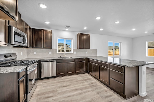 kitchen with kitchen peninsula, dark brown cabinets, light wood-type flooring, and stainless steel appliances