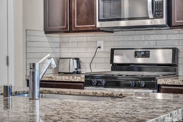 kitchen with light stone countertops, dark brown cabinets, backsplash, and stainless steel appliances