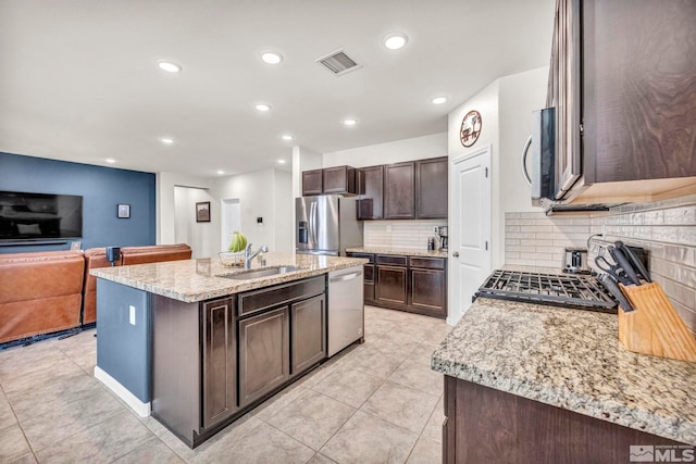 kitchen featuring a kitchen island with sink, sink, light stone countertops, dark brown cabinets, and stainless steel appliances