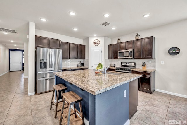 kitchen featuring backsplash, dark brown cabinetry, stainless steel appliances, sink, and an island with sink