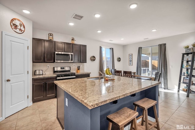 kitchen with backsplash, a breakfast bar, stainless steel appliances, a kitchen island with sink, and light tile patterned flooring