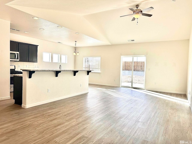 unfurnished living room with a textured ceiling, ceiling fan with notable chandelier, wood-type flooring, and vaulted ceiling