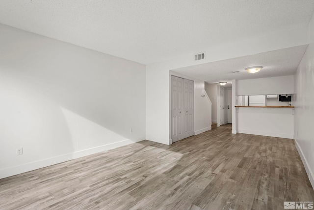 unfurnished living room with a textured ceiling and light hardwood / wood-style flooring