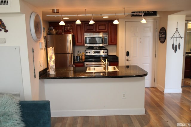 kitchen with sink, stainless steel appliances, kitchen peninsula, decorative light fixtures, and hardwood / wood-style flooring