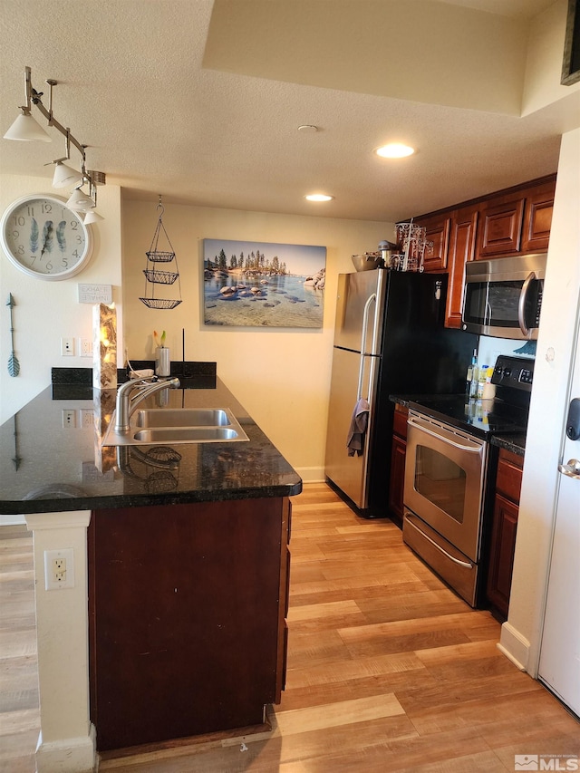 kitchen featuring sink, light hardwood / wood-style flooring, kitchen peninsula, a textured ceiling, and appliances with stainless steel finishes