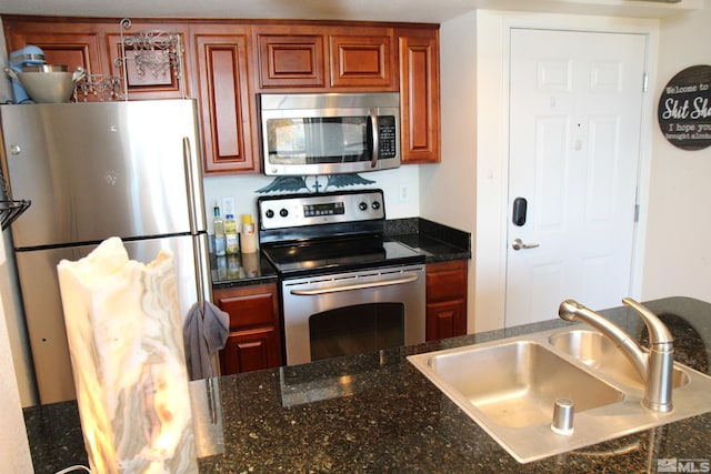 kitchen with stainless steel appliances, dark stone countertops, and sink