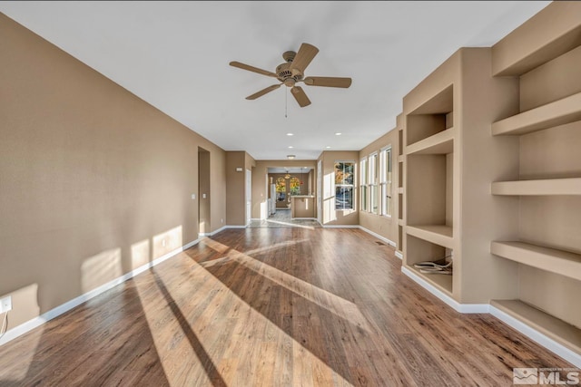 unfurnished room with ceiling fan, built in features, and wood-type flooring