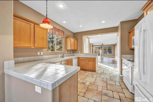 kitchen featuring kitchen peninsula, white appliances, sink, decorative light fixtures, and tile counters