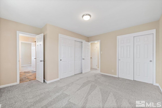 unfurnished bedroom featuring light carpet and two closets