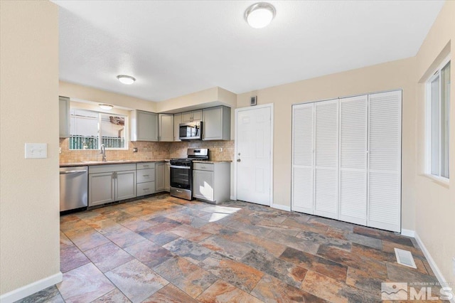 kitchen featuring backsplash, stainless steel appliances, gray cabinets, and sink