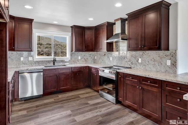 kitchen with hardwood / wood-style floors, wall chimney range hood, sink, light stone counters, and stainless steel appliances