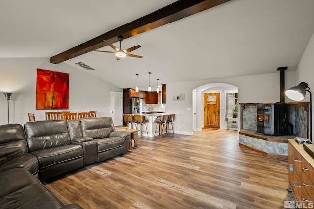 living room featuring a wood stove, ceiling fan, lofted ceiling with beams, and light wood-type flooring