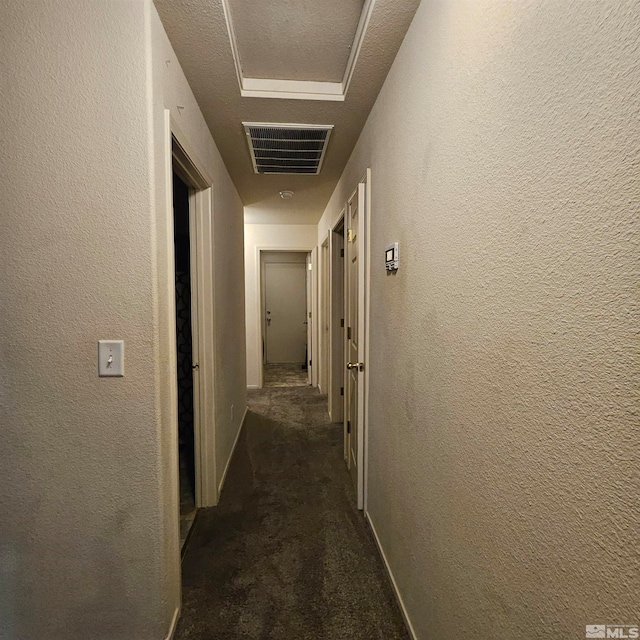 corridor with dark carpet and a textured ceiling