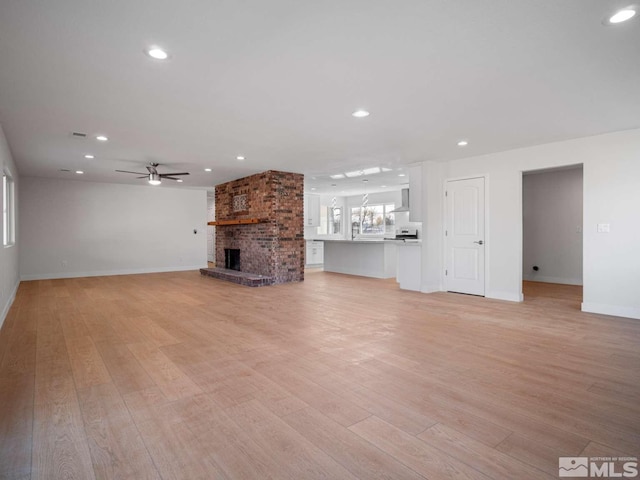 unfurnished living room with ceiling fan, a fireplace, and light wood-type flooring