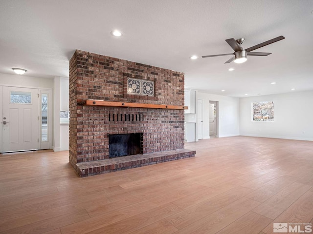 unfurnished living room with a textured ceiling, ceiling fan, light wood-type flooring, and a fireplace