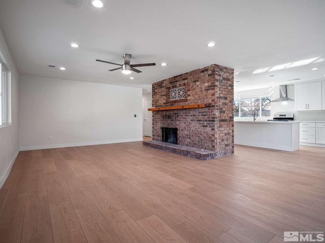 unfurnished living room with light hardwood / wood-style floors, a brick fireplace, and ceiling fan