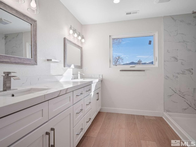 bathroom featuring a tile shower, vanity, and wood-type flooring