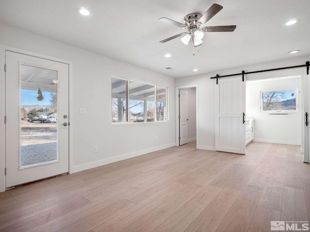 interior space with a barn door, ceiling fan, and light hardwood / wood-style flooring