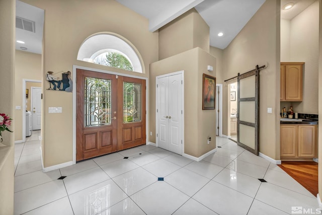 entryway with a barn door, light tile patterned floors, and a high ceiling