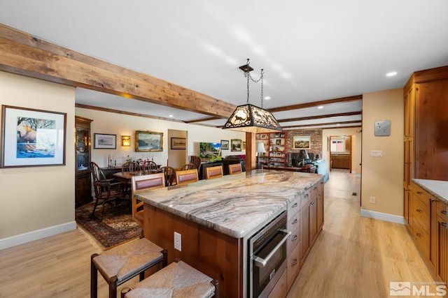 kitchen featuring beam ceiling, light stone countertops, a center island, pendant lighting, and light wood-type flooring