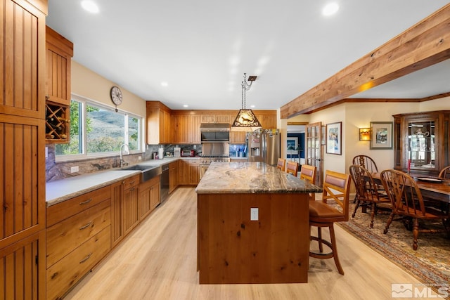 kitchen with a center island, sink, stainless steel appliances, hanging light fixtures, and light hardwood / wood-style flooring