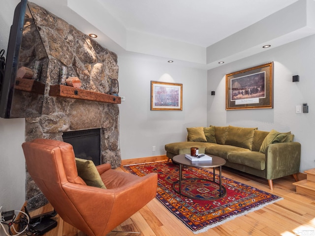 living area with a fireplace, recessed lighting, a raised ceiling, wood finished floors, and baseboards