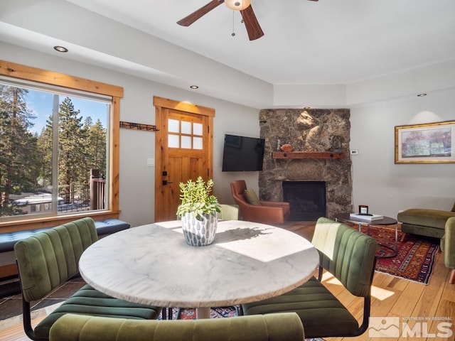 dining room with light wood-style floors, ceiling fan, and a stone fireplace