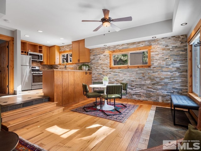 interior space with a ceiling fan, appliances with stainless steel finishes, wood finished floors, a peninsula, and open shelves