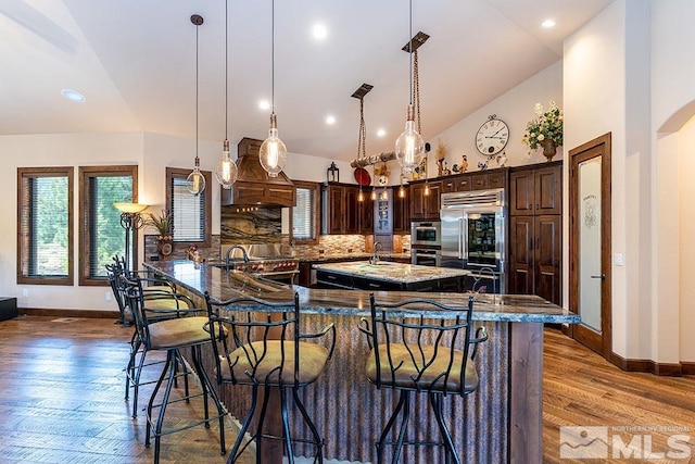 kitchen with backsplash, dark wood-type flooring, hanging light fixtures, dark brown cabinets, and stainless steel appliances