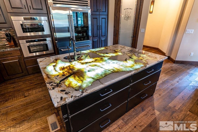 kitchen featuring a center island, light stone counters, dark hardwood / wood-style flooring, dark brown cabinetry, and stainless steel appliances