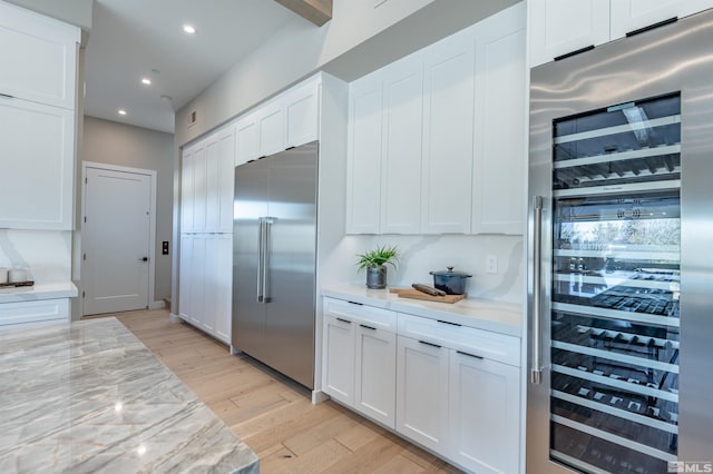 kitchen with wine cooler, white cabinets, stainless steel built in refrigerator, and light wood-type flooring