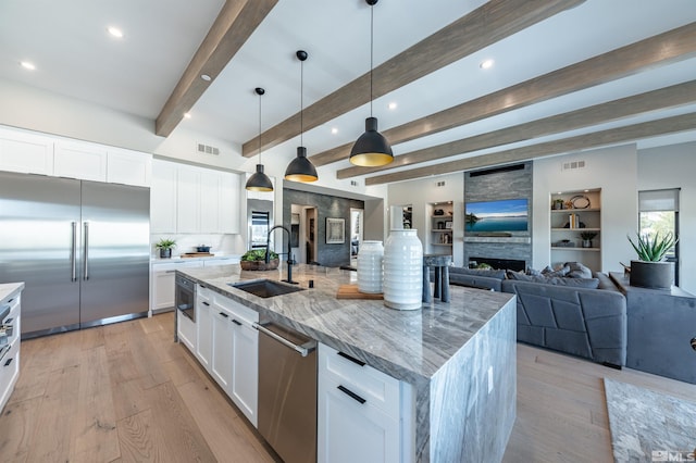 kitchen featuring a large island with sink, sink, appliances with stainless steel finishes, beamed ceiling, and white cabinetry