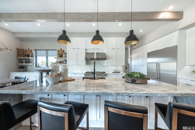 kitchen with light stone countertops, stainless steel appliances, a large island with sink, white cabinets, and hanging light fixtures