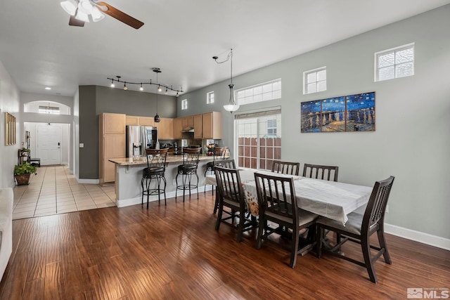 dining room with wood-type flooring, ceiling fan, and a high ceiling