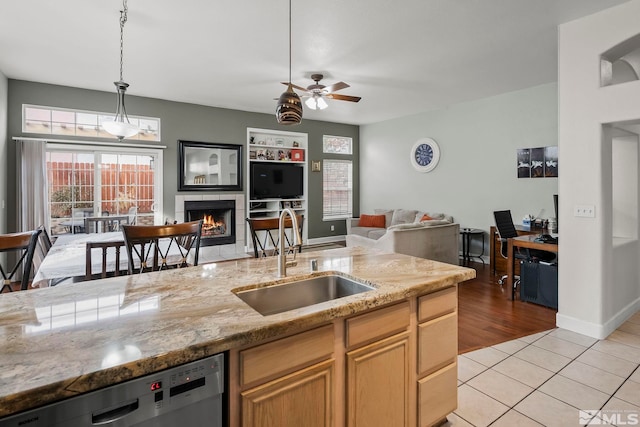 kitchen with light wood-type flooring, stainless steel dishwasher, ceiling fan, sink, and a tiled fireplace