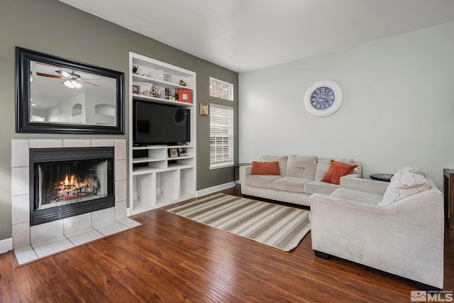 living room with a tiled fireplace, ceiling fan, wood-type flooring, and vaulted ceiling