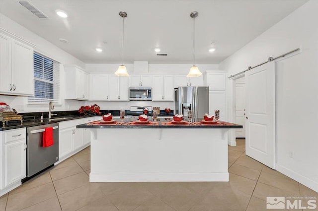 kitchen with pendant lighting, a center island, white cabinets, a barn door, and stainless steel appliances