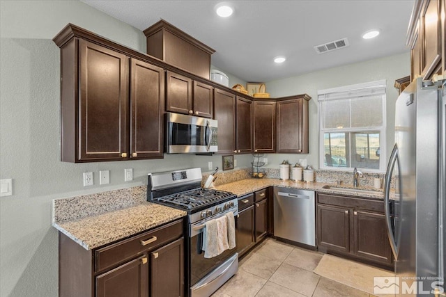 kitchen with sink, light tile patterned floors, dark brown cabinets, light stone counters, and stainless steel appliances