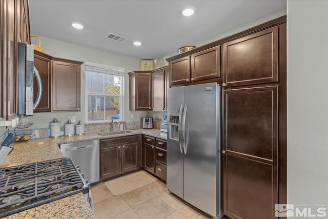 kitchen with light stone countertops, sink, stainless steel appliances, and dark brown cabinets