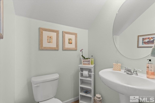 bathroom with a textured ceiling, vaulted ceiling, toilet, and sink