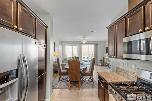 kitchen with dark brown cabinetry, ceiling fan, stainless steel appliances, light stone counters, and light tile patterned flooring