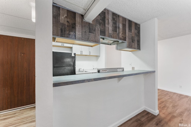 kitchen featuring white cabinetry, sink, kitchen peninsula, black refrigerator, and light wood-type flooring