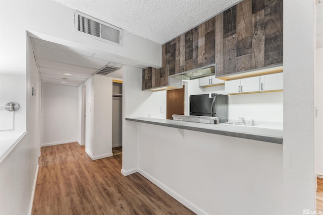 kitchen with black refrigerator, kitchen peninsula, sink, dark hardwood / wood-style floors, and white cabinetry